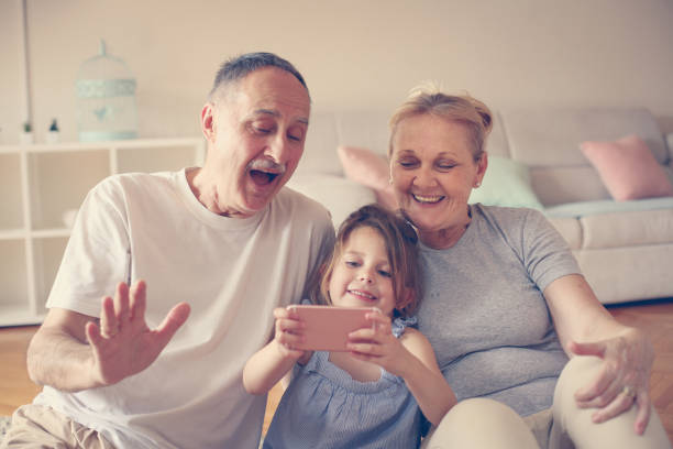grandmother and grandfather with their granddaughter using smart phone. - wireless technology cheerful granddaughter grandmother imagens e fotografias de stock