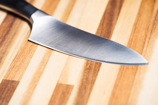 A close-up of the blade of a sharp kitchen knife, on a laminated chopping baord.