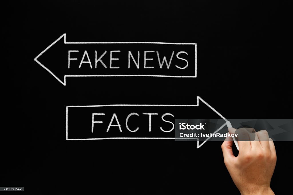 Fake News Or Facts Arrows Concept Hand sketching Fake News or Facts concept with white chalk on blackboard. Artificial Stock Photo