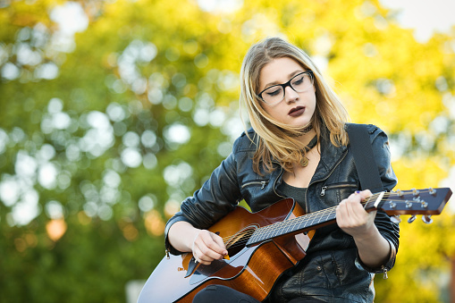 A beautiful 15 year old girl playing an acoustic guitar outdoors.