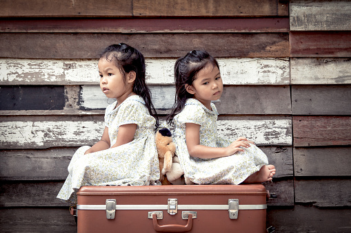 children two cute asian little girls are sitting on suitcase and playing together on wooden background in vintage retro style