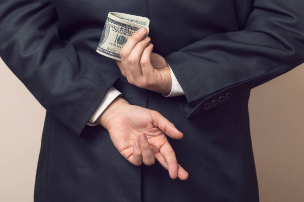 Embezzlement Businessman in a suit holding his hands behind his back with stack of dollar banknotes in one and fingers crossed on another one bluff stock pictures, royalty-free photos & images