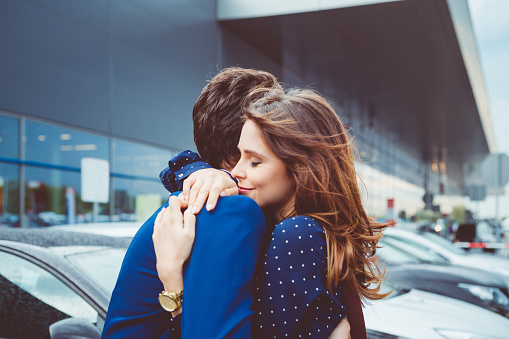Loving young couple say good bye at airport, man and woman embracing at car parking lot.