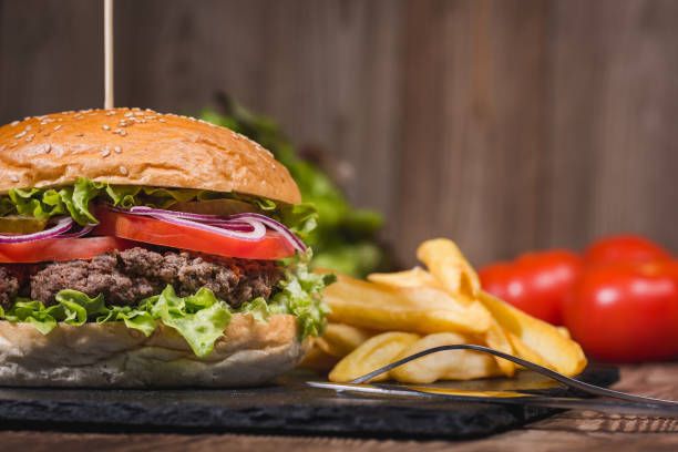 istock Classic burger on wooden table with vegetables on the background. 681149190