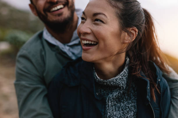 Couple enjoying on vacation Smiling asian woman being embraced by her boyfriend from behind. Couple enjoying on vacation. common couple men outdoors stock pictures, royalty-free photos & images