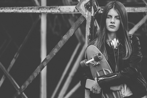 Teenage girl in melancholy mood holding skateboard