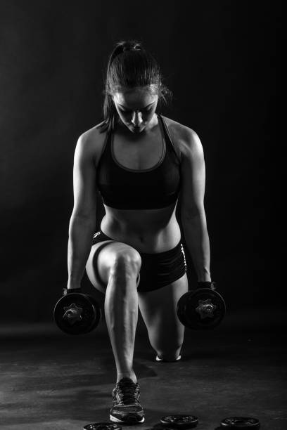 istock Woman bodybuilder lifting dumbbell isolated over black background, Black and white. 681264474