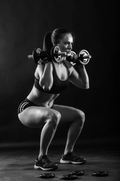 Woman bodybuilder lifting dumbbell isolated over black background, Black and white.