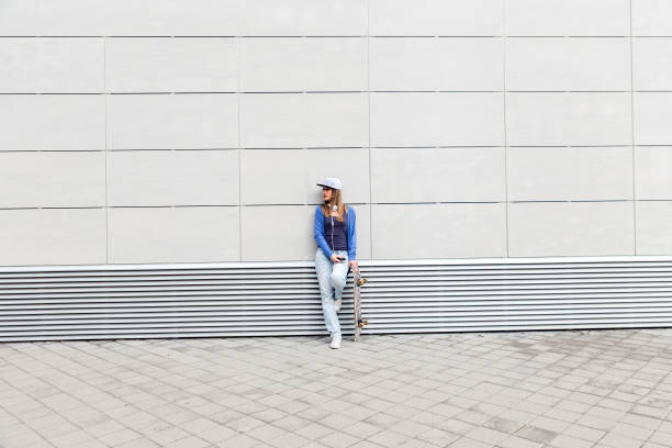 istock Young girl with skateboard leaning on modern gray wall. 681272080