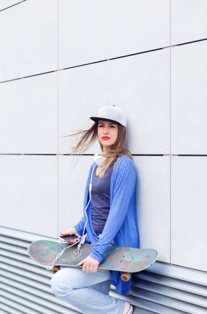 istock Young girl with skateboard leaning on modern gray wall. 681273424