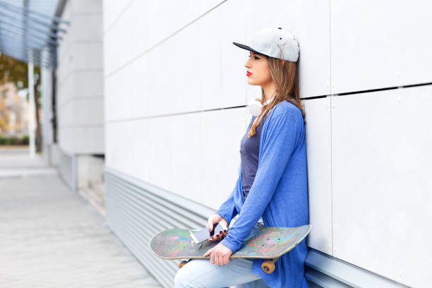 istock Young girl with skateboard leaning on modern gray wall. 681274730