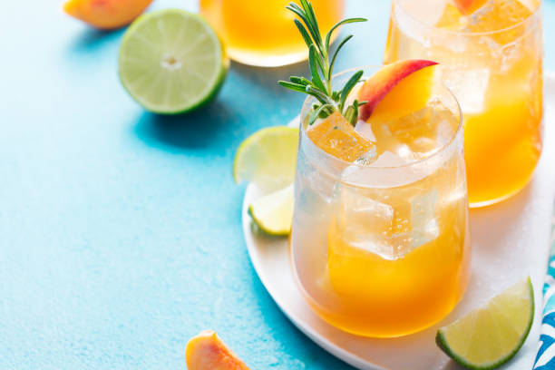 peach cocktail, fizz, ice tea with fresh rosemary and lime. blue background. copy space. - peach juice imagens e fotografias de stock