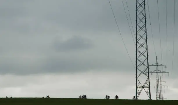 Silhouettes of cyclists next to high-voltage pylons