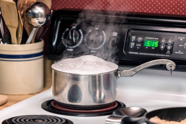 Boiling Water Pasta Pot Overflowing on Stove Top Burner The boiling water in a steaming hot family size pasta cooking pot is overflowing on a home kitchen electric stove top burner. overflowing stock pictures, royalty-free photos & images