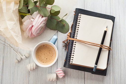 Top view of open blank notebook, bouquet, flower, cup of coffee, earphones. Travel and adventure concept, journey diary