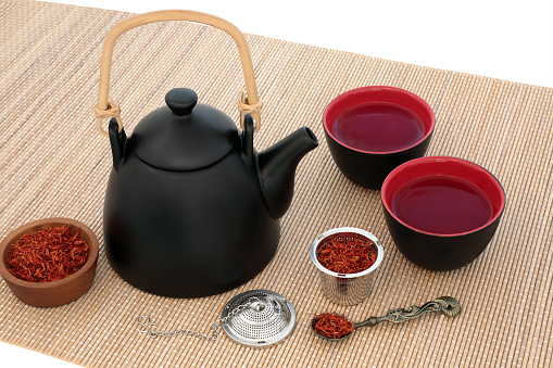 Safflower herb tea with oriental teapot and cups with strainer and old spoon on bamboo over white background. Used also in chinese herbal medicine.