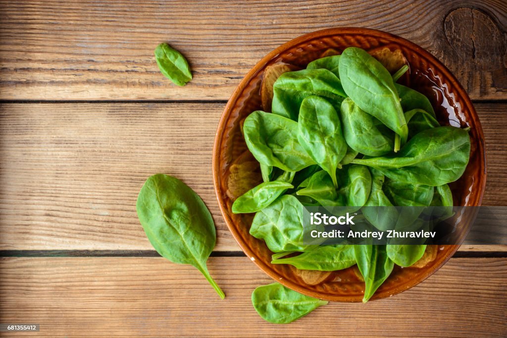 Fresh spinach leaves in bowl on rustic wooden table. Fresh spinach leaves in bowl on rustic wooden table. Top view. Agriculture Stock Photo
