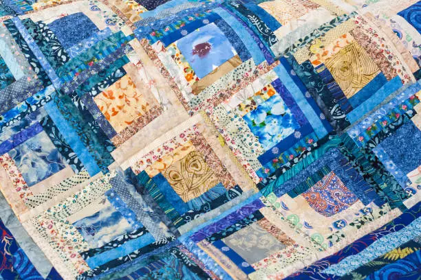 patchwork, handmade, sewing, interior, home cosiness concept - colourful folksy quilt in blue shades made of ornate snippets with floral prints stitched together in form of squares