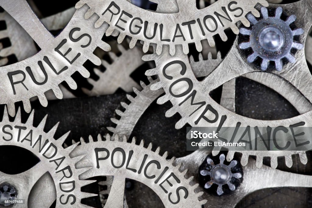 Metal Wheel Concept Macro photo of tooth wheels with COMPLIANCE, REGULATIONS, STANDARDS, POLICIES and RULES words imprinted on metal surface Law Stock Photo