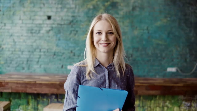 Portrait of successful beautiful blonde businesswoman at loft coworking space. Female holds the document, smiling