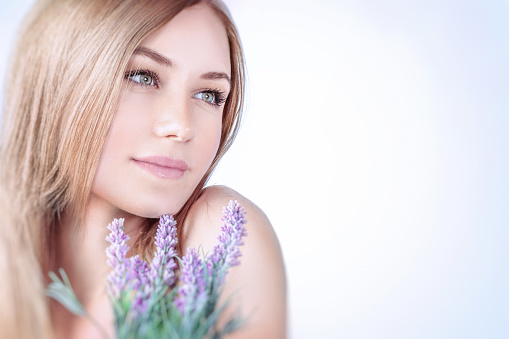 Beautiful woman at spa, closeup portrait of a nice blond girl enjoying aroma of a lavender flowers over clear background, using natural cosmetics, healthy lifestyle