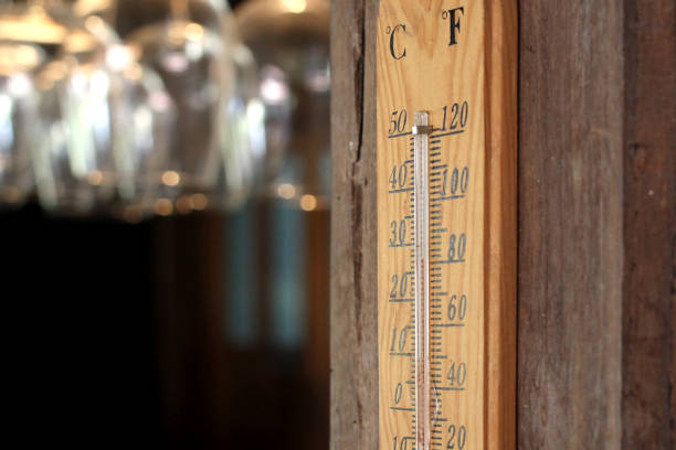 Thermometer reading 90 degrees Fahrenheit with out of focus corn and hay fields in the background in rural Appalachia