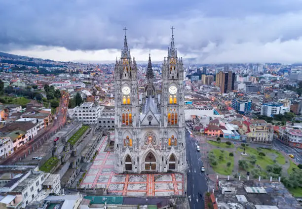 Aerial perspective of the beautiful Basílica del Voto Nacional at sunset with the typical clouds hanging over Quito, the capital of Ecuador. The city and church lights have just been illuminated.