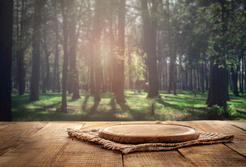 Round wood board on a wooden table on a forest background for product montage