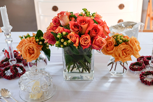 Gorgeous floral arrangements placed in 3 vases in the center of dining table on top of white table cloth.