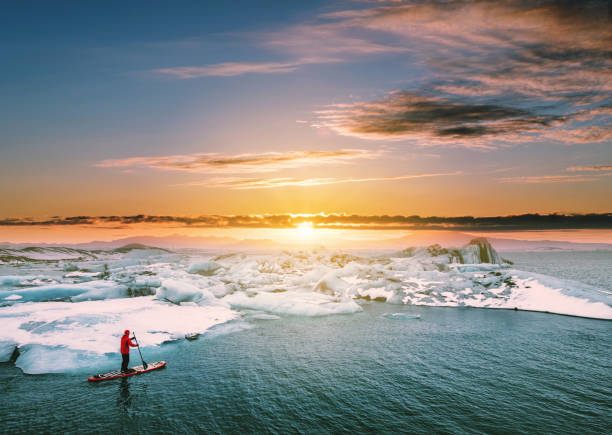 Landscaped, Beautiful glacier lagoon in sunset with a guy paddle boarding