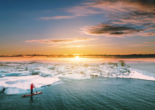 Landscaped, Beautiful glacier lagoon in sunset with a guy paddle boarding Landscaped, Beautiful glacier lagoon in sunset with a guy paddle boarding polar climate photos stock pictures, royalty-free photos & images