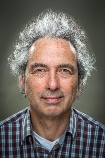 Portrait of real happy, blissful man, with grey, wild hair, uncombed looking straight in the camera, big smile on grey background
