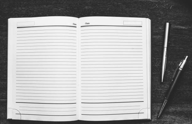 Black and white photo. Notebook with pens on the old wood table