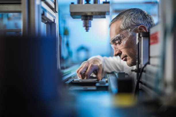 Quality control worker analyzing scientific experiment on a manufacturing machine. Mid adult male engineer examining machine part on a production line in a factory. innovation technology stock pictures, royalty-free photos & images