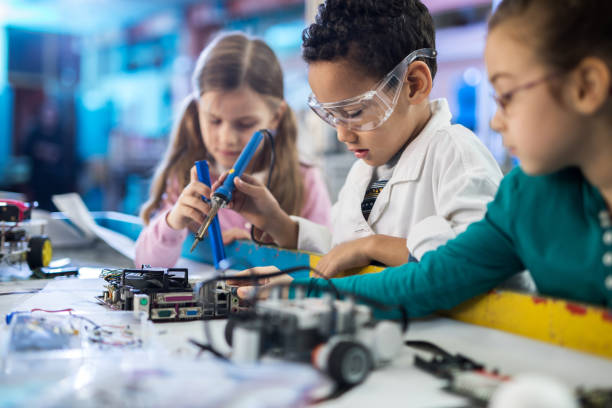 Team of small engineers working on a computer part in laboratory. Group of little children working with soldering iron on a computer part in laboratory. Focus is on boy. school science project stock pictures, royalty-free photos & images