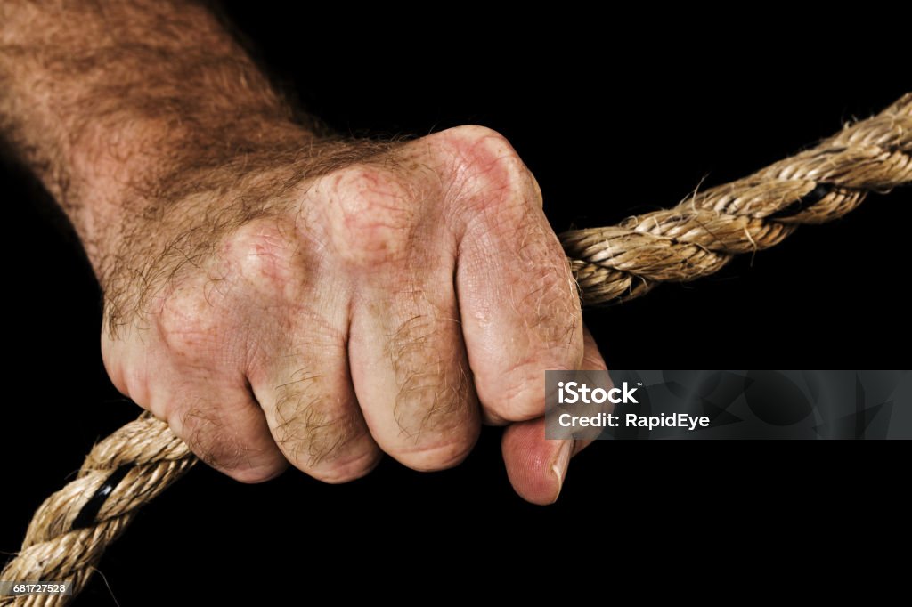 Masculine hand grips rope, holding fast. Black background. A man's hand pulls on a heavy-duty rope against a black background. Black Background Stock Photo