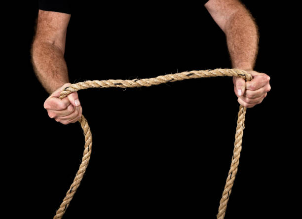 istock Masculine hands grip rope, pulling apart. Black background. 681727666
