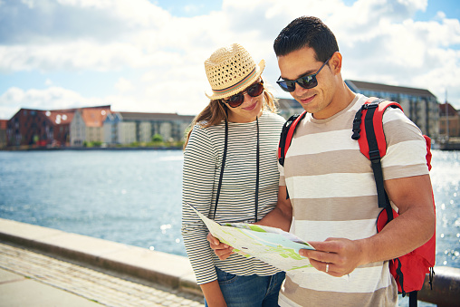 Young couple enjoying their summer vacation at the seaside standing on a waterfront promenade looking for directions on a map