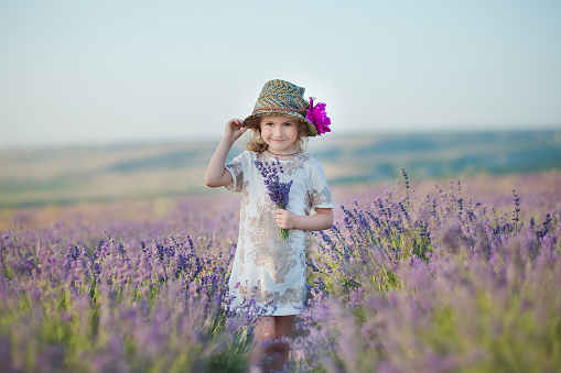 Young beautiful girl walking on the lavender field on a weekend day in wonderful dresses and hats