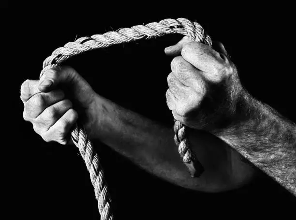 Masculine hands grip a heavy-duty rope, pulling to the sides. Black and white image.