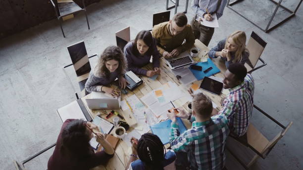 istock Business meeting at loft shared space. Multiethnic team talking, woman manager giving direction to people. Top view 681735286