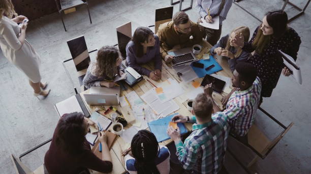 istock Business meeting at loft shared space. Multiethnic team talking, woman manager giving direction to people. Top view 681735348