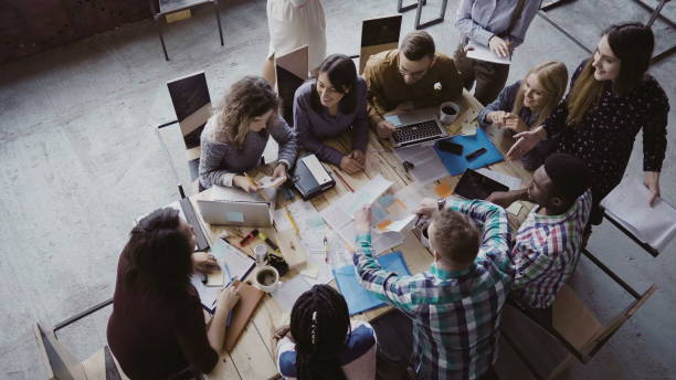 istock Business meeting at loft shared space. Multiethnic team talking, woman manager giving direction to people. Top view 681735366