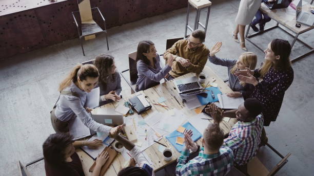 draufsicht der kreative business-teams arbeiten im modernen büro. kollegen reden, lächeln, hohe fünf miteinander - meeting community board room leadership stock-fotos und bilder