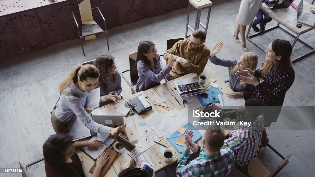 Top view of creative business team working at modern office. Colleagues talking, smiling, high five with each other Top view of creative business team working at loft modern office. Colleagues talking, smiling, high five with each other. Happy young start-up project, brainstorming in boardroom. Crowdfunding Stock Photo