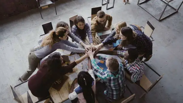 Photo of Top view of business team working at trendy loft office. Young mixed race group of people puts palm together on centre