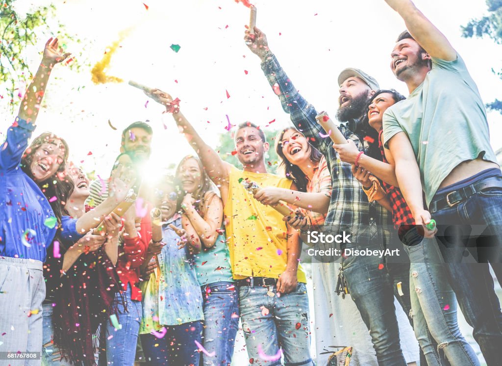 Amici felici che si godono la festa, lanciano coriandoli e usano i colori delle bombe fumogene alla festa all'aperto - Foto stock royalty-free di Party