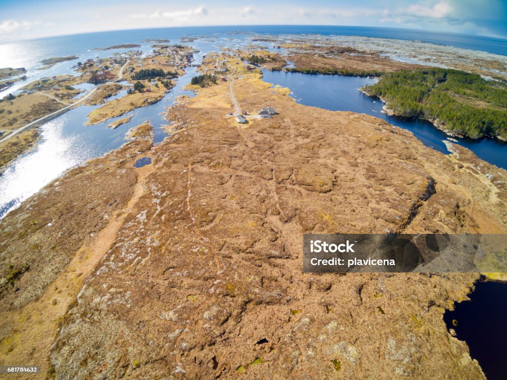 Fishing village, around rocky terrain covered with grass Titran, Norway - April 15, 2017: Aerial view from flying drone. Rocky island, moss and grassland. The banks of the fjord, blue water. Turistic buildings, a fishing village in the background. Hitra Stock Photo