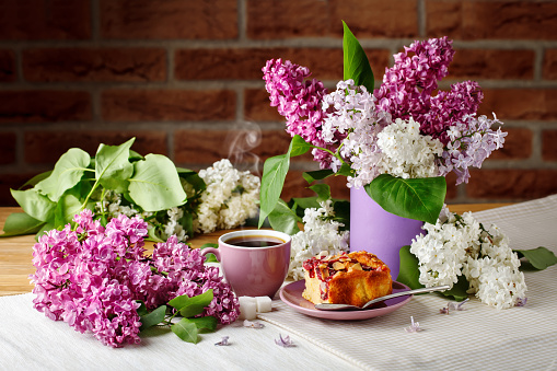 Still life with branches of lilac and a Cup of coffee and cake on a wooden table.