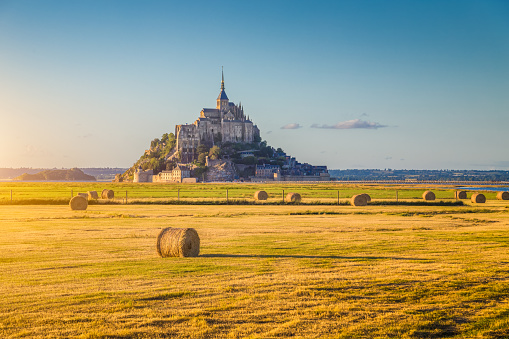 Beautiful view of famous historic Le Mont Saint-Michel in golden evening light at sunset in summer with hay bales on fields with retro vintage Instagram style pastel filter effect, Normandy, France